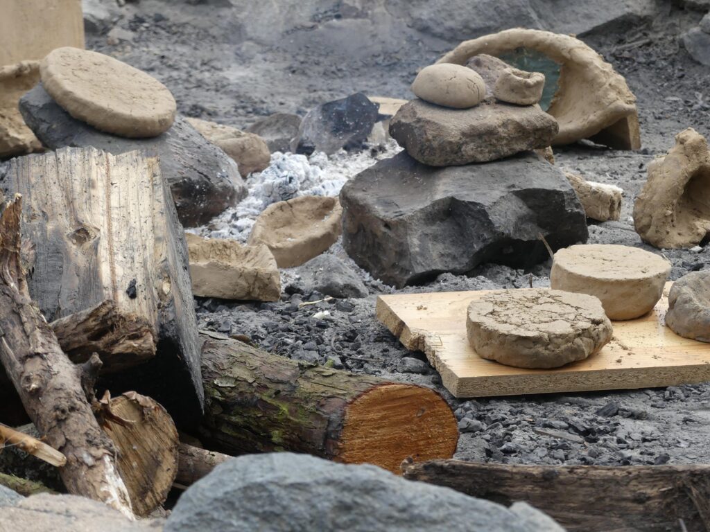 Selbst gebackene Fladenbrote liegen auf Steinen und einem Holzbrett in der Asche einer Feuerstelle beim Steinzeit-Camp
